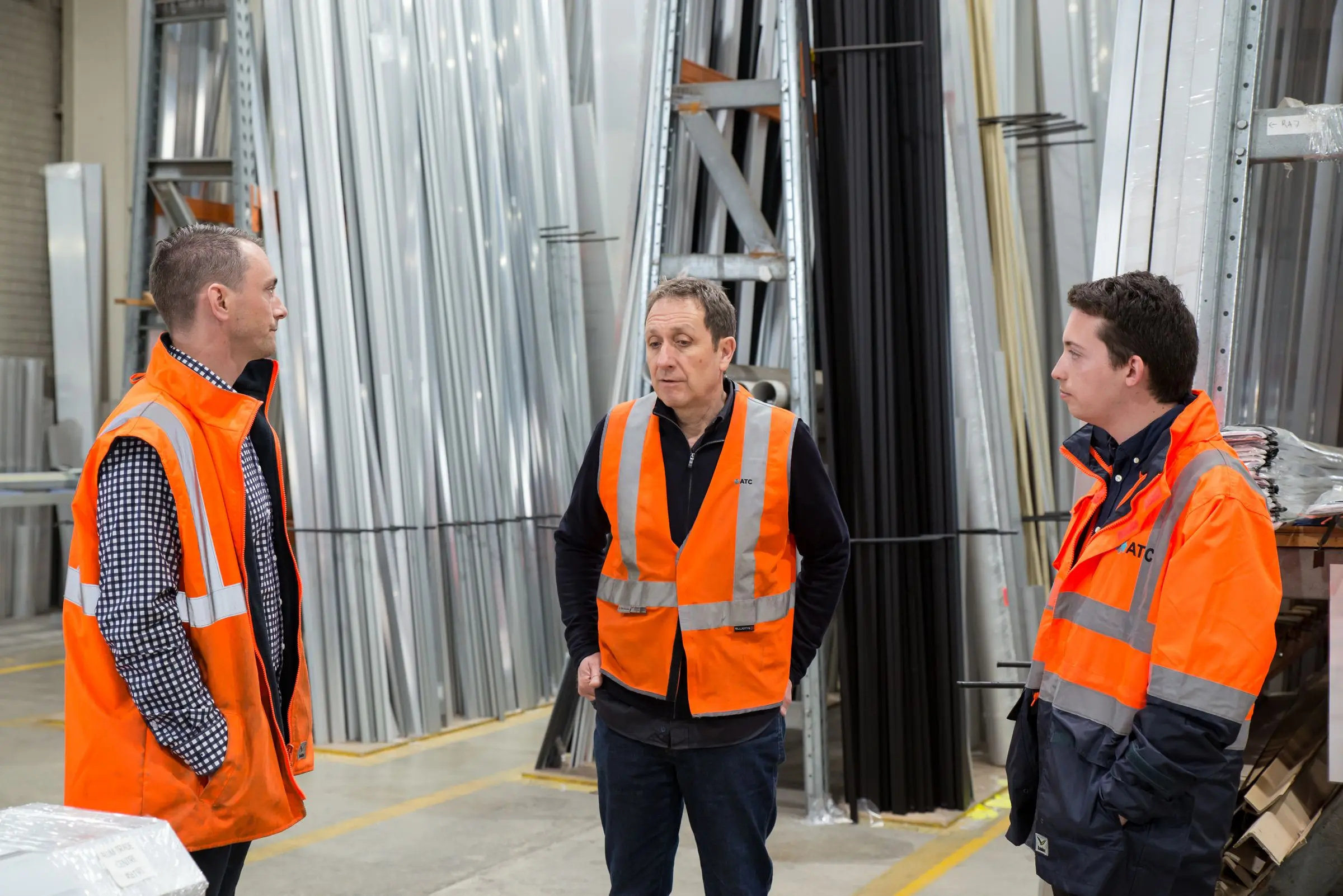 Three managers in safety vests talking on the plant floor
